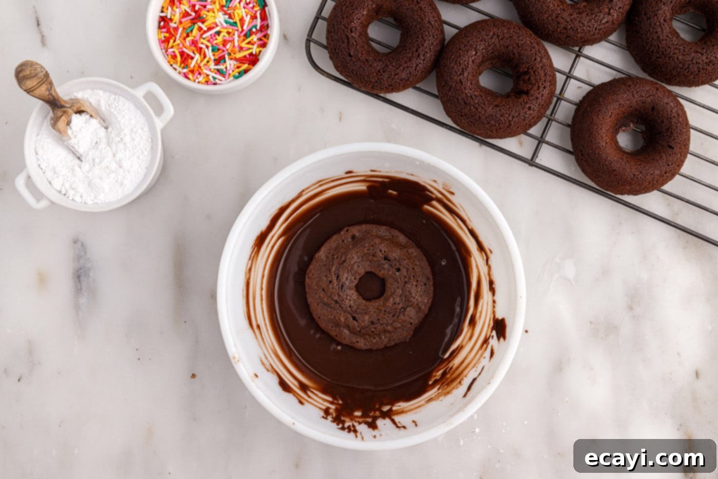 ChocoRings 16 dipping a baked bronut into a bowl of chocolate glaze, coating the top surface