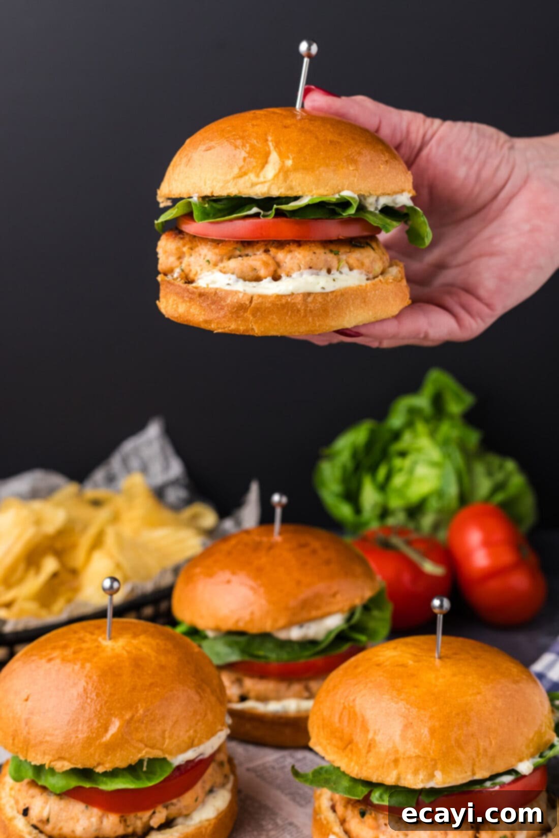 Delicious Salmon Burgers 13 Hand holding up a cooked Salmon Burger above a tray of more burgers, ready to be served
