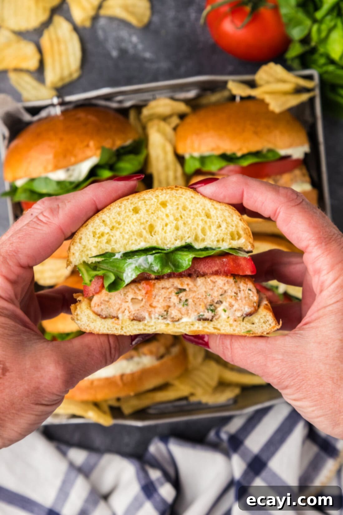 Delicious Salmon Burgers 3 Hands holding up a half of a Salmon Burger with fresh tomato, lettuce, and bun