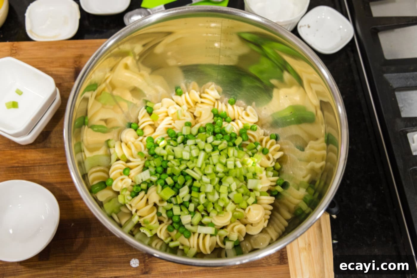 Lemon-Herb Shrimp Pasta Salad 6 Chopped celery and peas being added to a large bowl with cooked rotini pasta, forming the base of the salad.