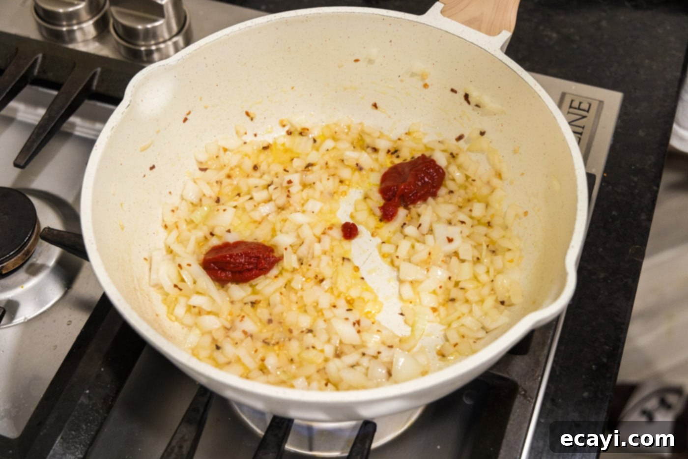 Creamy Vodka Pasta Sauce 6 tomato pasta being added to a skillet of sautéed onion and garlic mixture