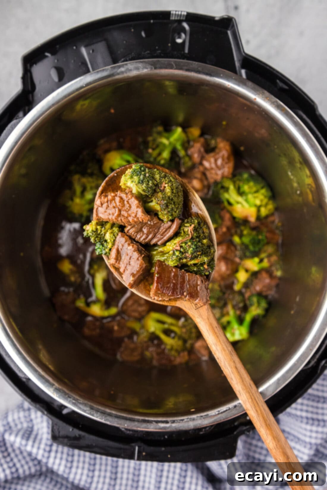 Delicious Instant Pot Beef and Broccoli 12 A serving spoon gracefully lifts a generous portion of Instant Pot Beef and Broccoli, showcasing the rich sauce and tender ingredients, held above the open Instant Pot.