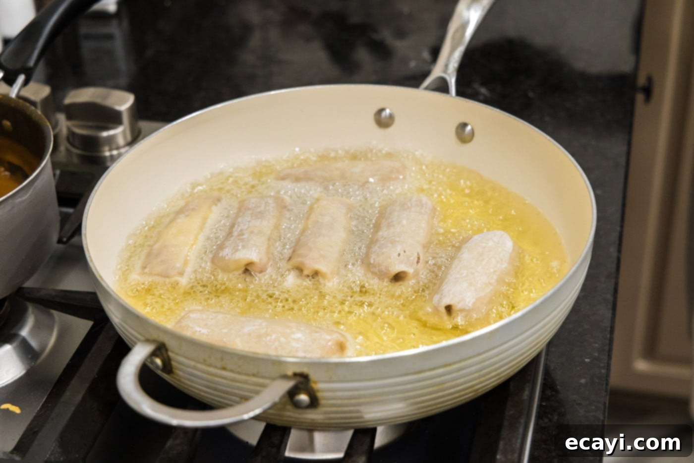 Crispy Reuben Egg Rolls 12 Several Reuben egg rolls sizzling and turning golden brown in hot oil in a deep skillet during the frying process.
