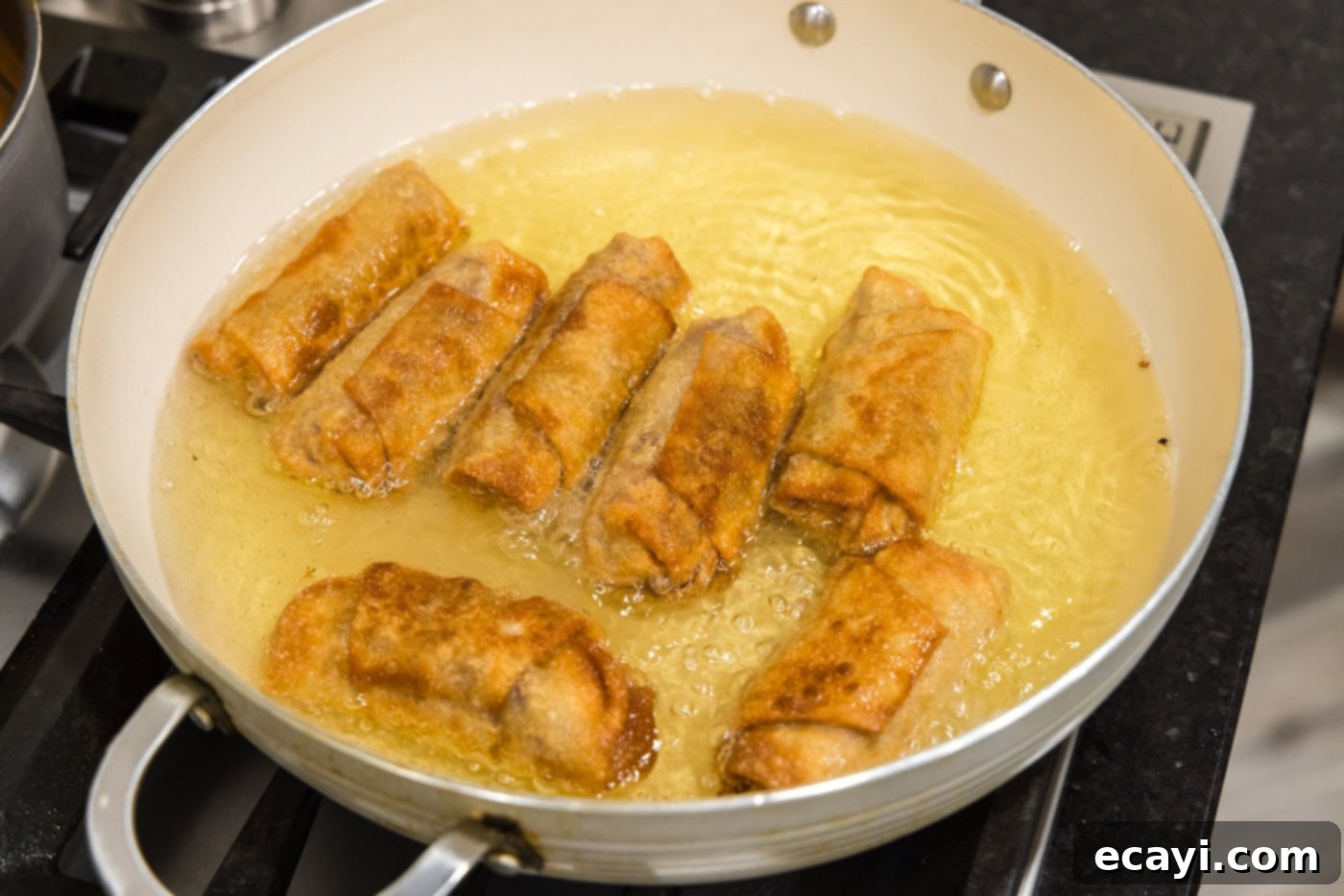 Crispy Reuben Egg Rolls 13 Freshly fried, golden brown Reuben egg rolls being removed from a skillet of hot oil with tongs.
