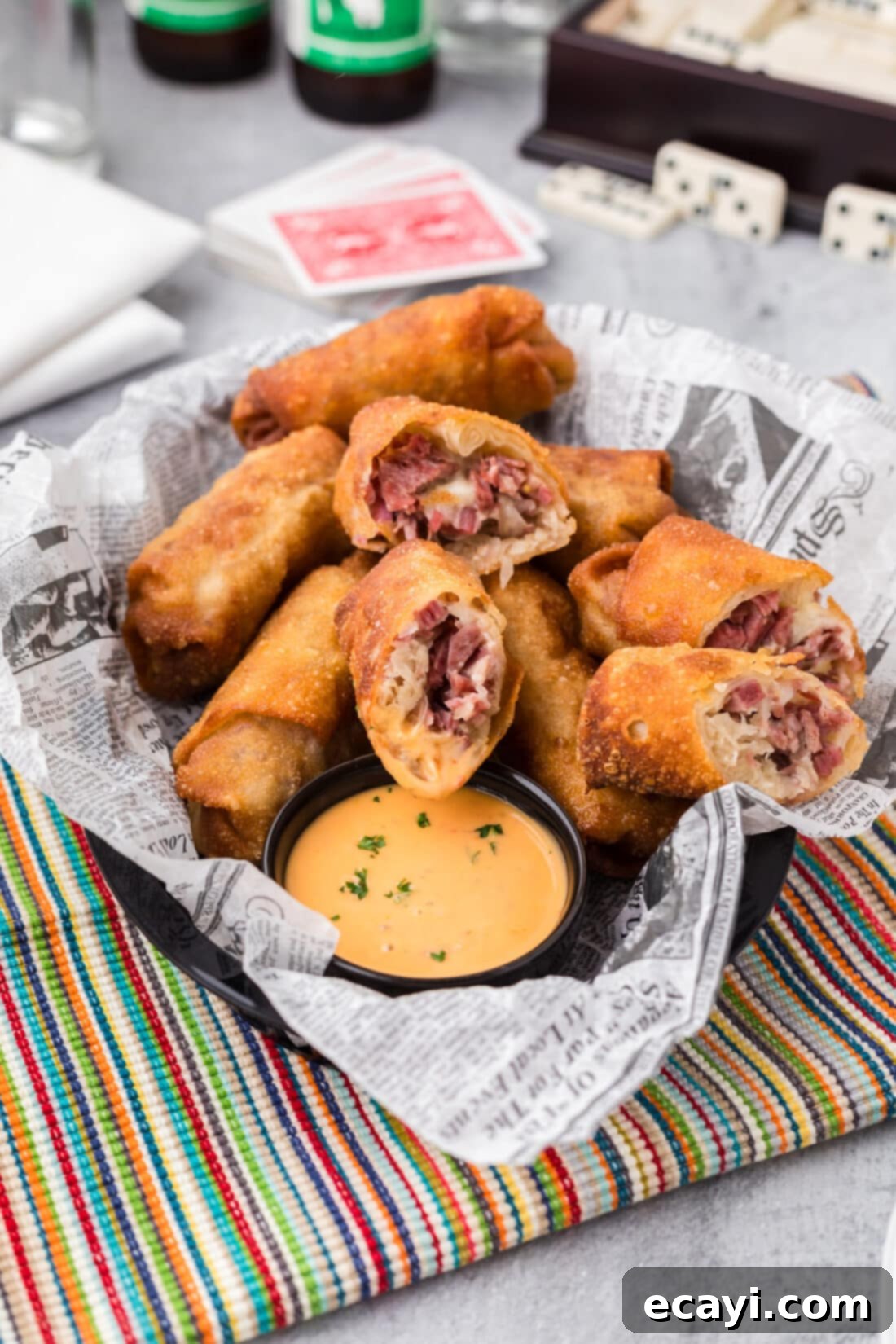 Crispy Reuben Egg Rolls 14 A rustic basket filled with golden-brown Reuben Egg Rolls cut in half, showcasing the flavorful filling, with a small bowl of dipping sauce on the side.