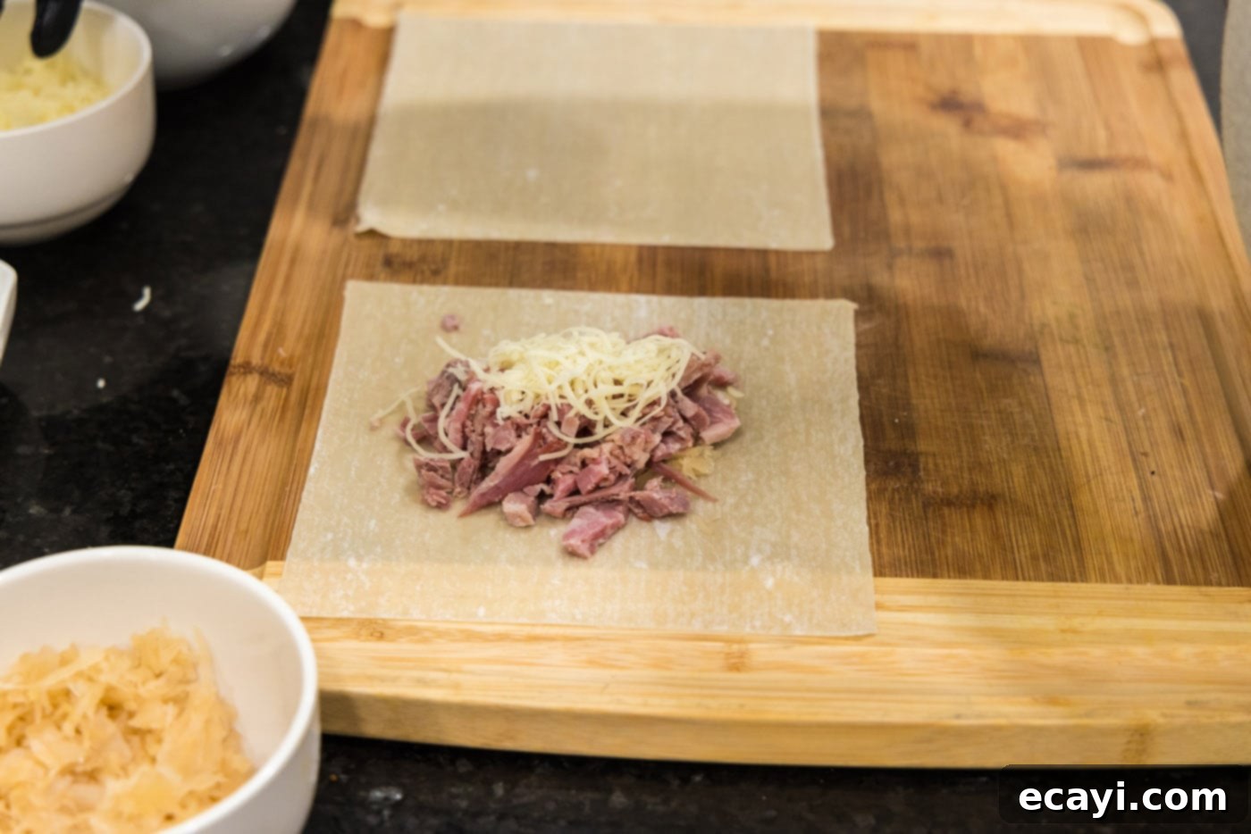 Crispy Reuben Egg Rolls 6 An egg roll wrapper with a neat pile of chopped corned beef and shredded Swiss cheese on top of sauerkraut, ready for folding.