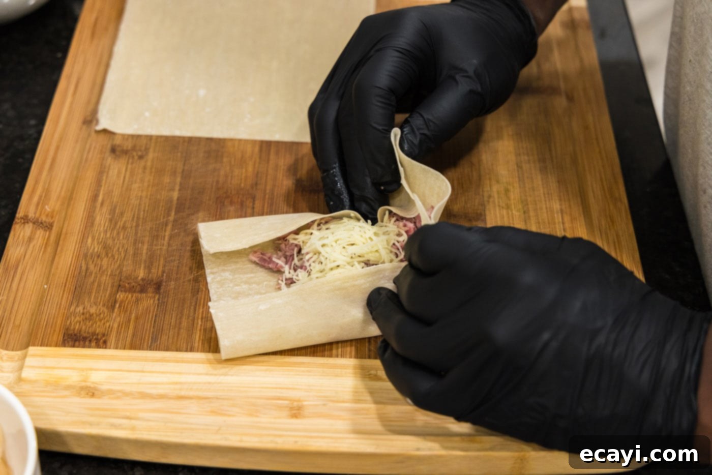 Crispy Reuben Egg Rolls 7 Hands demonstrating the folding process of an egg roll wrapper, with the bottom flap folded over the corned beef and Swiss cheese filling.