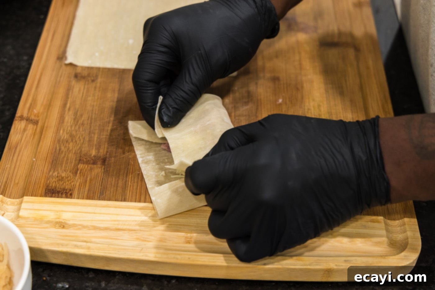 Crispy Reuben Egg Rolls 8 A close-up of hands applying water to the edge of an egg roll wrapper to seal it, mid-folding process.