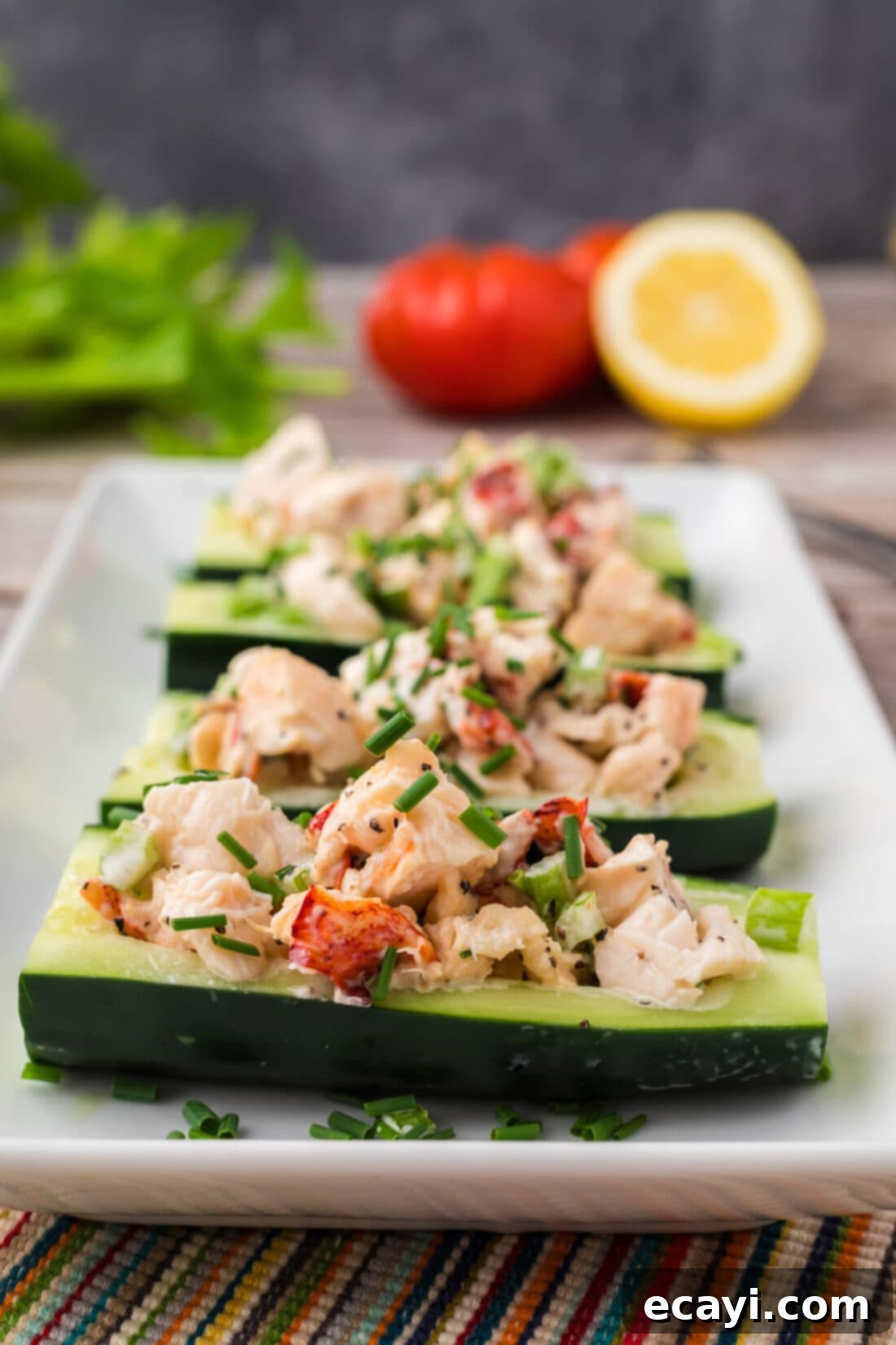 Chilled Lobster Cucumber Canoes 2 Close-up photo of vibrant Lobster Cucumber Boats, showcasing plump lobster meat, fresh celery, and chives in a creamy mayo dressing nestled in crisp cucumber halves, garnished with fresh herbs.