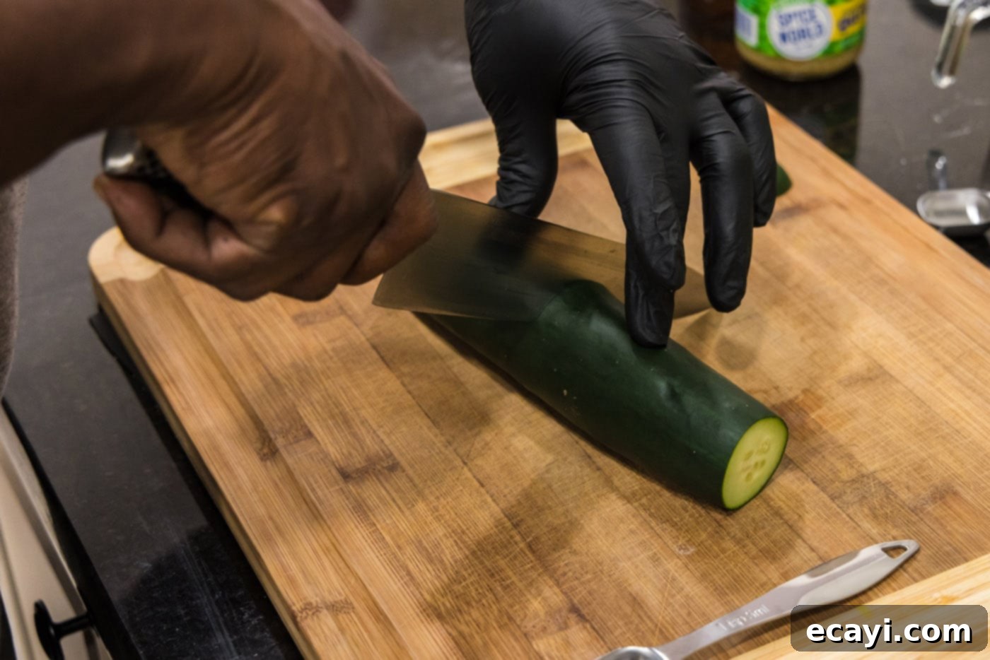Chilled Lobster Cucumber Canoes 9 A hand expertly slicing a fresh cucumber with a chef's knife on a clean cutting board, demonstrating the initial cut to prepare it for the boat shape.