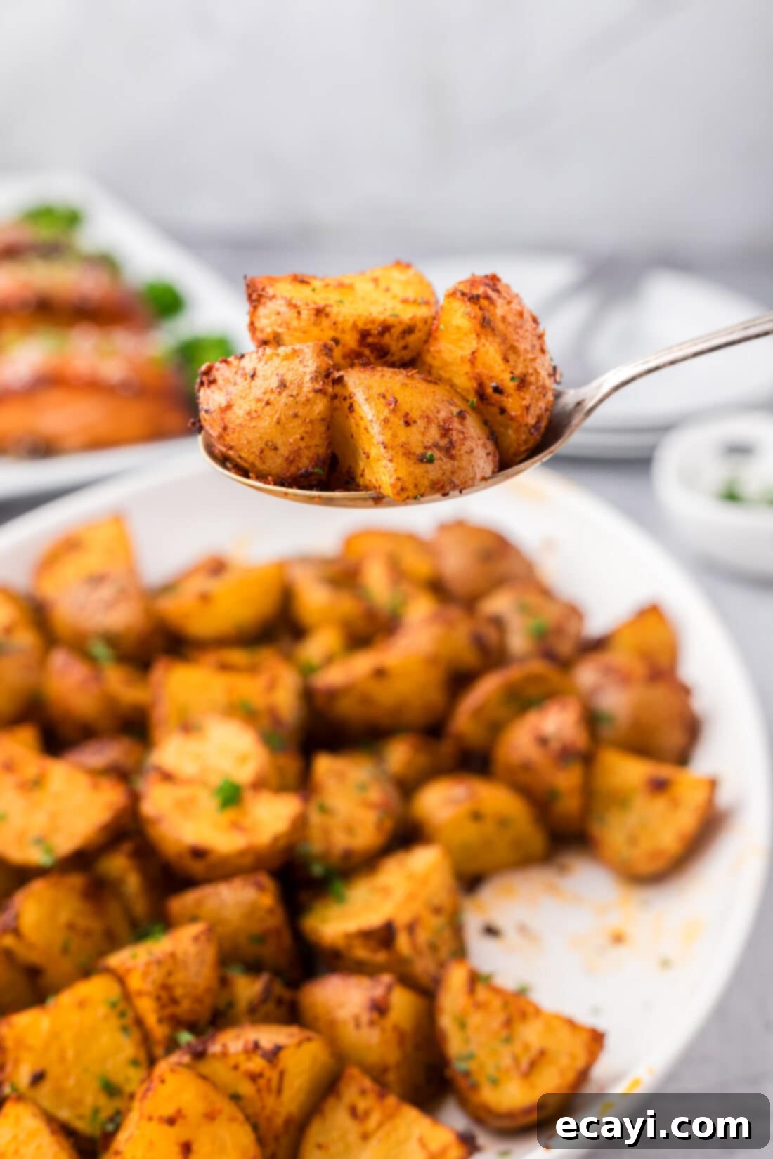 Fiery Roasted Potatoes 3 Spoonful of Spicy Potatoes held above a platter of Spicy Potatoes