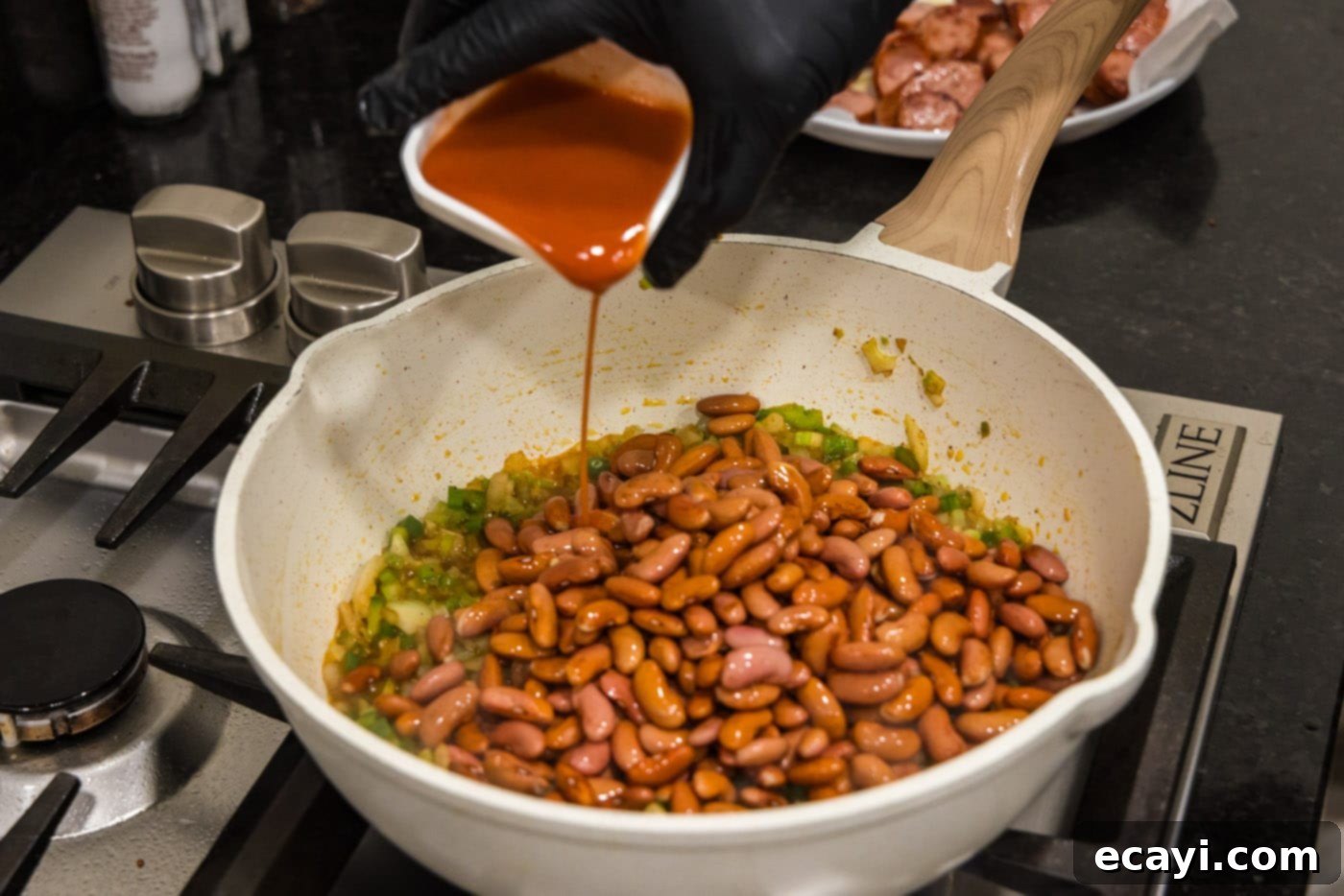 Hearty Louisiana Red Beans and Rice 8 pouring hot sauce into skillet with red beans and sautéed vegetables