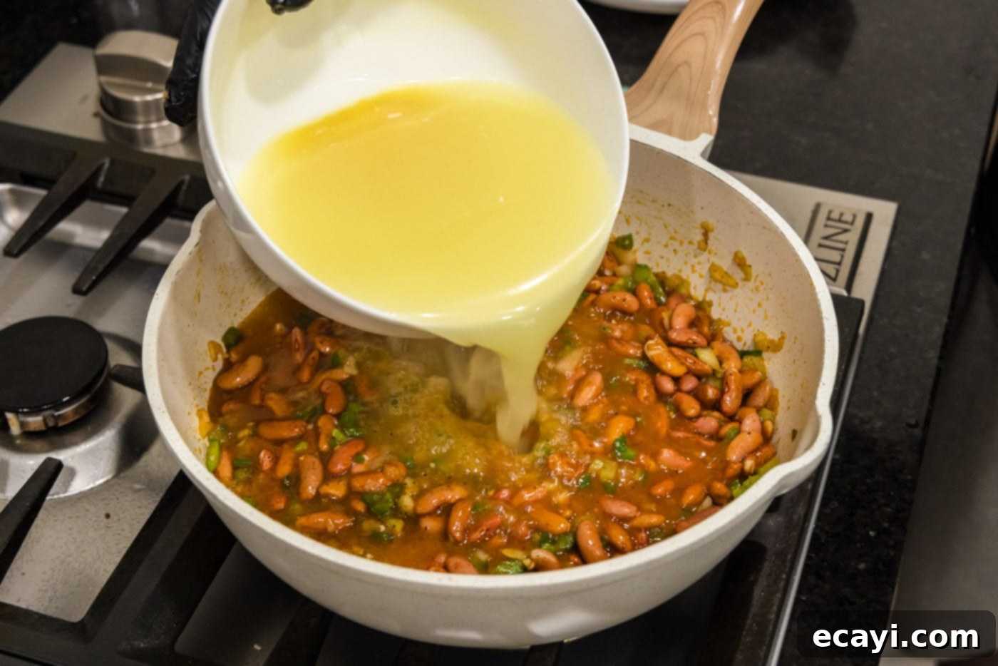Hearty Louisiana Red Beans and Rice 9 pouring chicken broth into skillet with red beans and sauteed vegetables