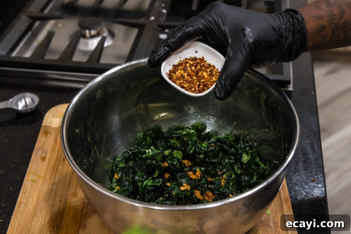 Crispy Spinach Sauté 10 Red pepper flakes being sprinkled generously over fried spinach and garlic in a bowl.