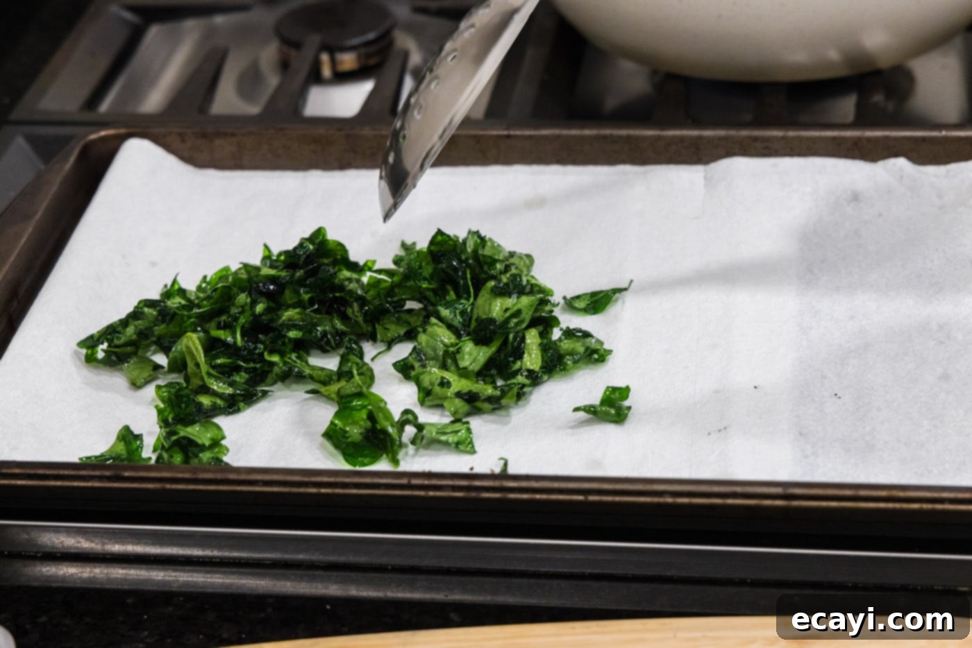 Crispy Spinach Sauté 8 A slotted spoon lifting crispy fried spinach from hot oil to drain on paper towels.