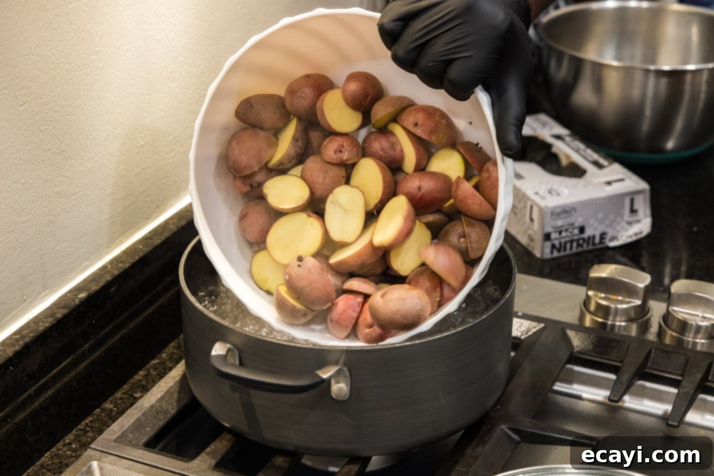 Creamy Garlic Mash 5 Adding perfectly halved baby red potatoes into a large pot of vigorously boiling water, creating a gentle splash.