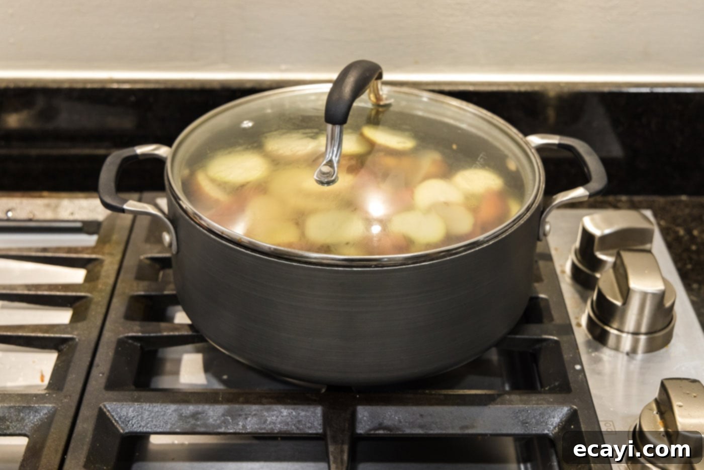Creamy Garlic Mash 6 A large pot of baby red potatoes simmering gently on a stovetop with the lid slightly ajar, steam gently rising.