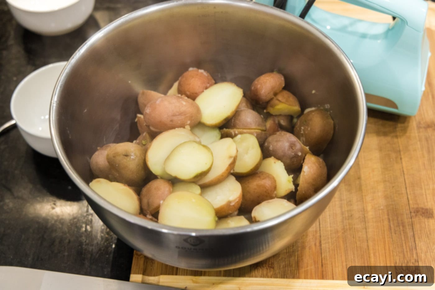 Creamy Garlic Mash 7 Steaming, cooked sliced red potatoes resting in a large metal mixing bowl, freshly drained and ready for the next step.