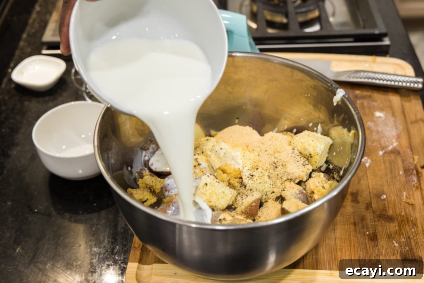 Creamy Garlic Mash 10 A stream of rich heavy whipping cream being poured into a bowl containing cooked potatoes, sour cream, butter, and roasted garlic, creating a swirl of white and yellow.