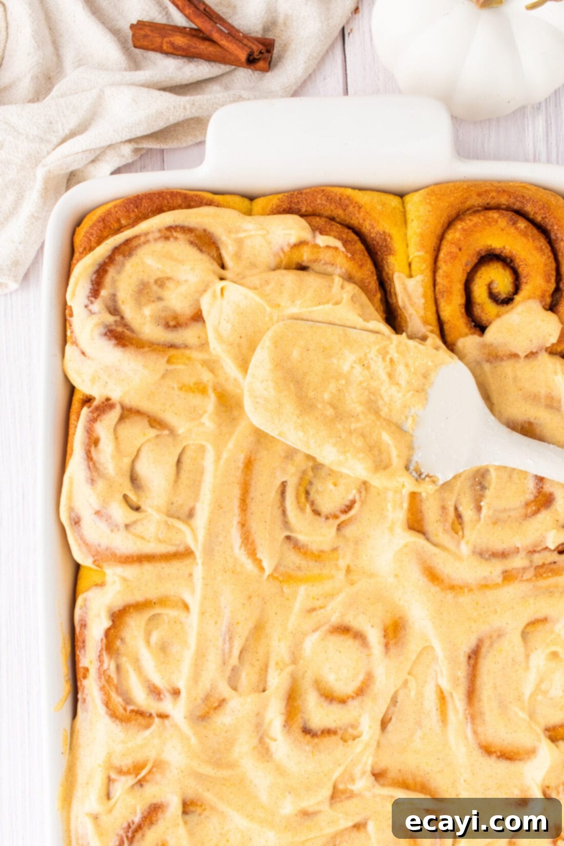 Golden Pumpkin Spiced Swirls 3 Frosting being spread onto freshly baked Pumpkin Cinnamon Rolls, showcasing the smooth texture