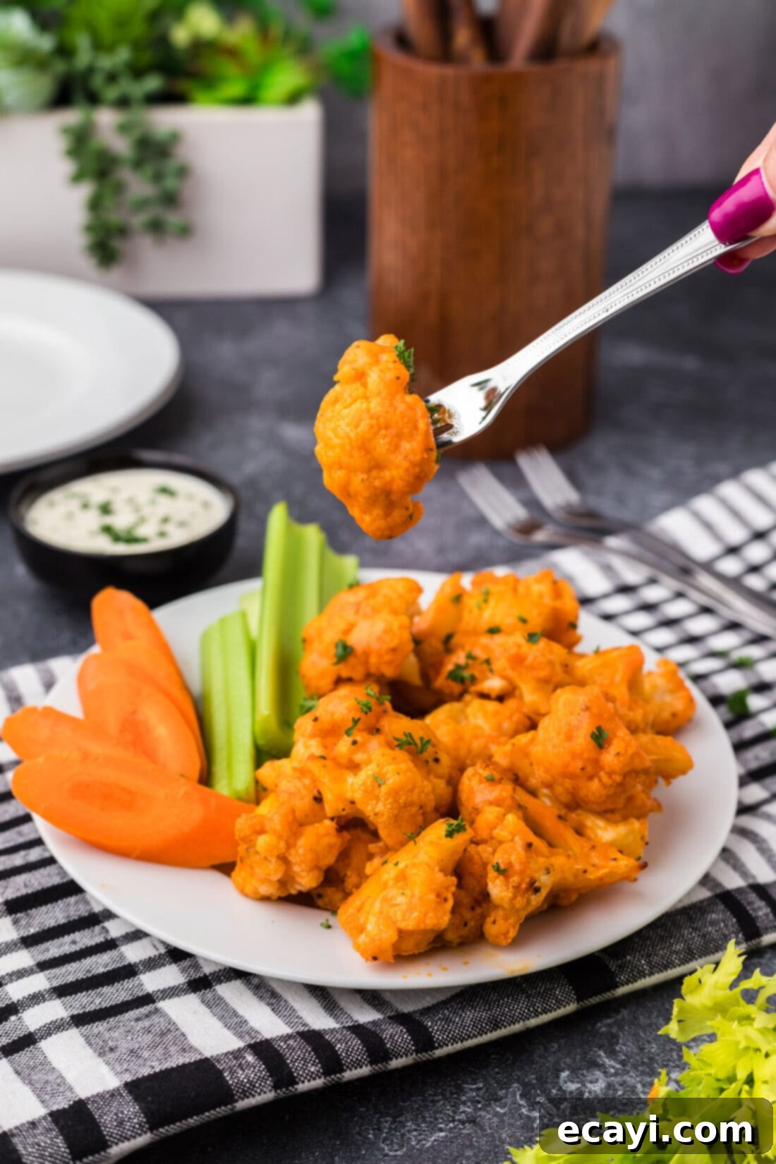 Buffalo Cauliflower Bites 3 Buffalo Cauliflower on a fork held above a plate of Buffalo Cauliflower, showing crispy texture