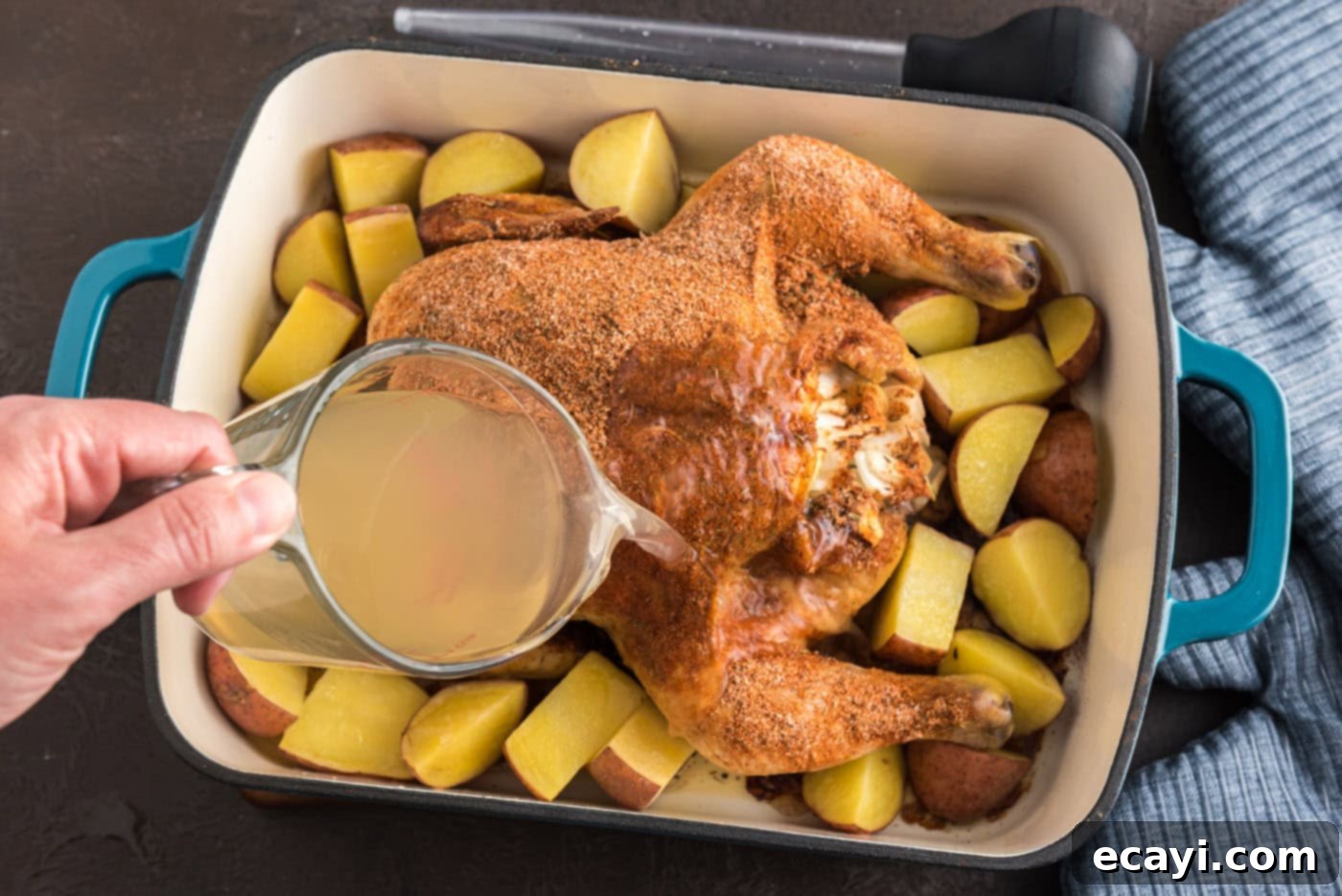 Slow Roasted Caramelized Chicken 8 pouring chicken stock over whole roasted chicken in pan with potatoes