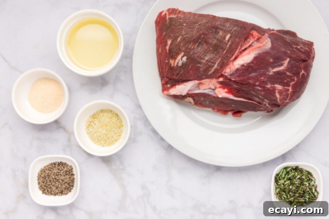 Perfect Air Fryer Roast Beef 4 A beautiful flat lay of all the essential ingredients needed for Air Fryer Roast Beef, including a raw sirloin tip roast, a bottle of olive oil, fresh rosemary, garlic salt, onion powder, and whole black peppercorns.