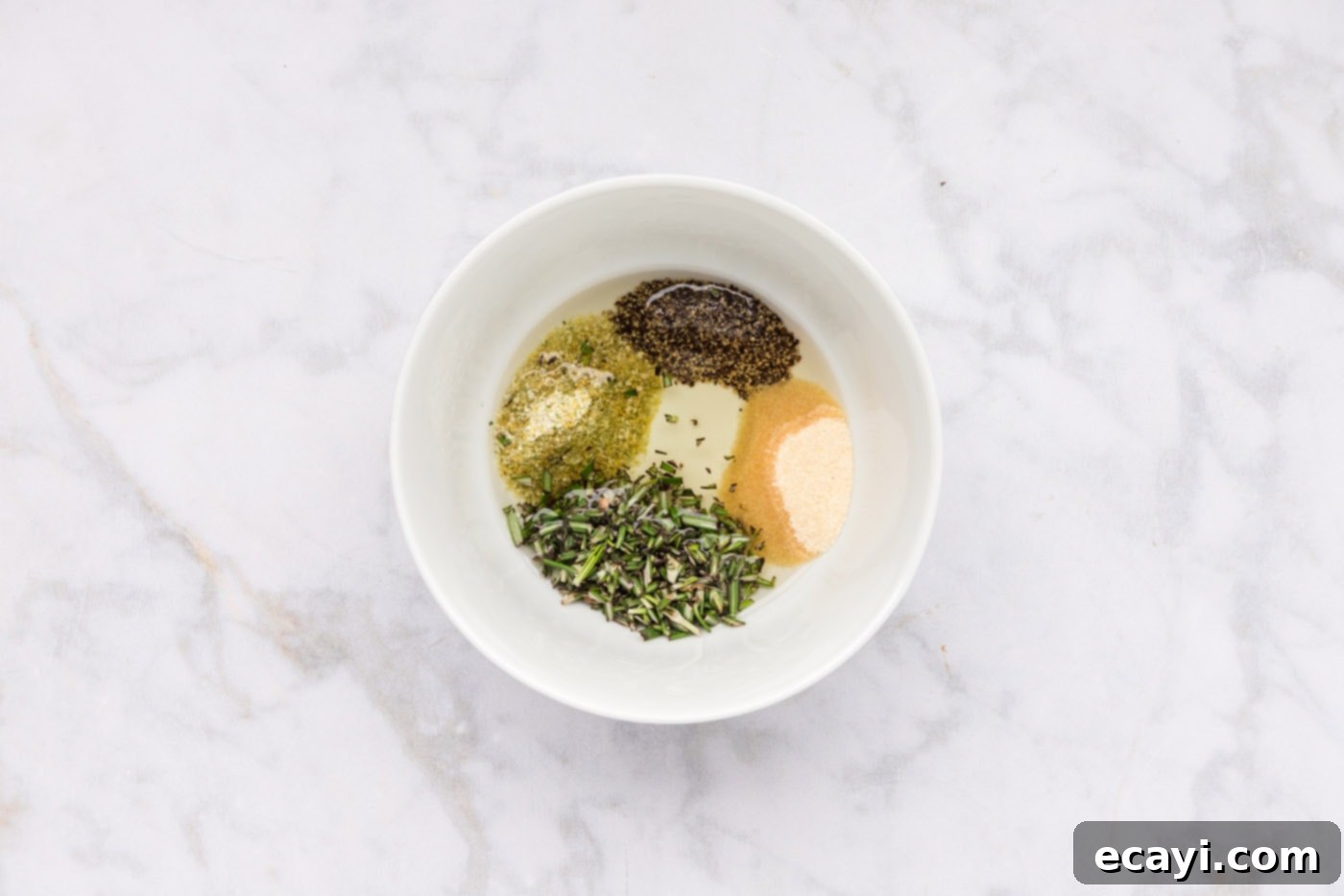 Perfect Air Fryer Roast Beef 5 A medium bowl containing olive oil, black pepper, garlic salt, onion powder, and fresh rosemary leaves, ready to be thoroughly whisked into a savory rub.
