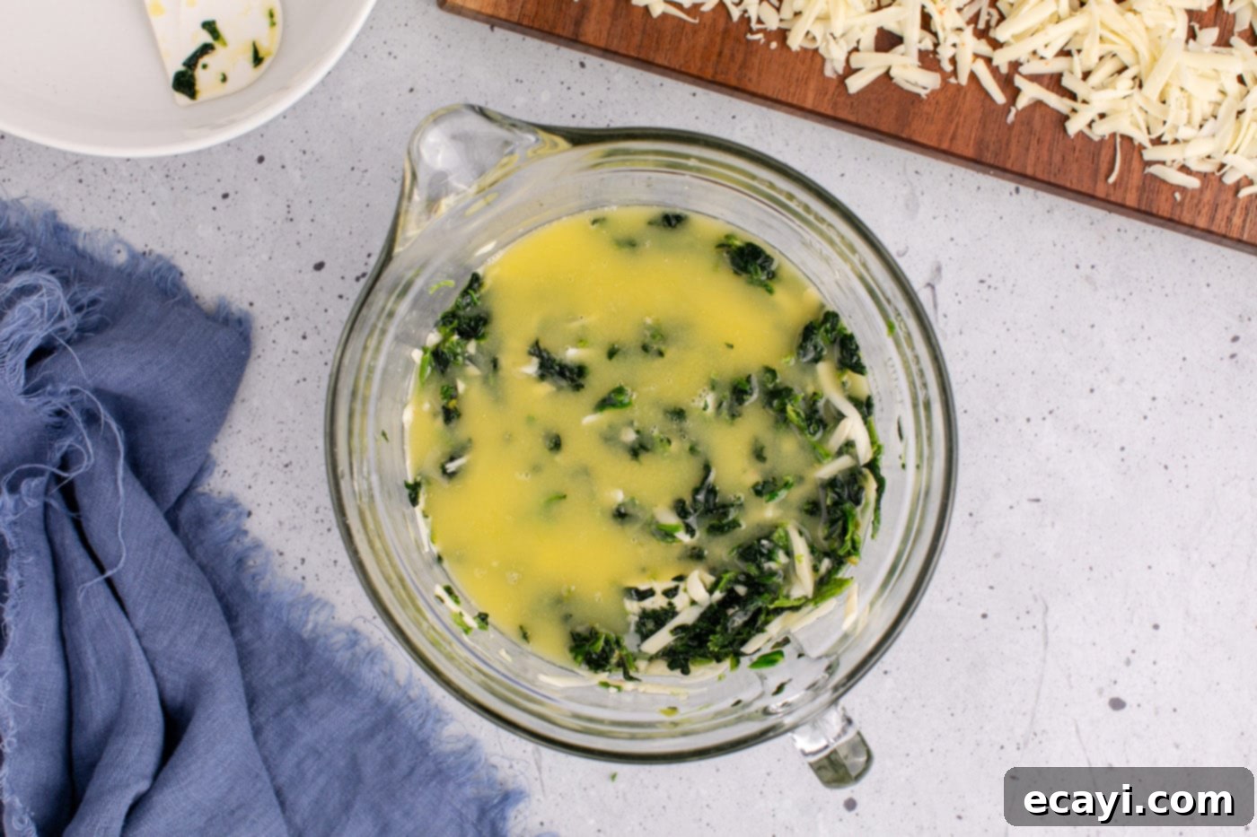 Savory Spinach Cloud 8 A stream of melted butter being poured over the spinach souffle mixture in a mixing bowl, adding richness and flavor.