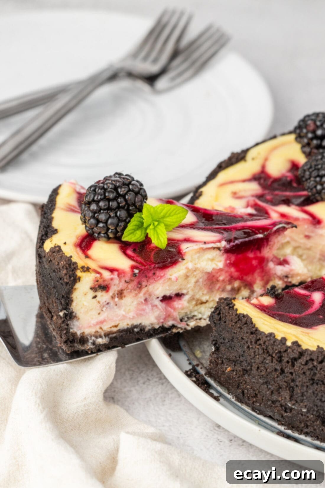 Blackberry Swirl Cheesecake 16 Slice of Blackberry Swirl Cheesecake being lifted away from the whole cheesecake