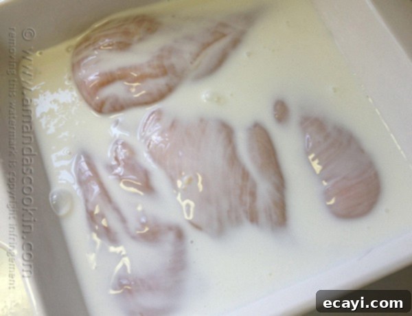 Golden-Crisp Oven Chicken Breasts 6 A close up photo of raw chicken breasts soaking in a bath of creamy buttermilk in a glass dish.