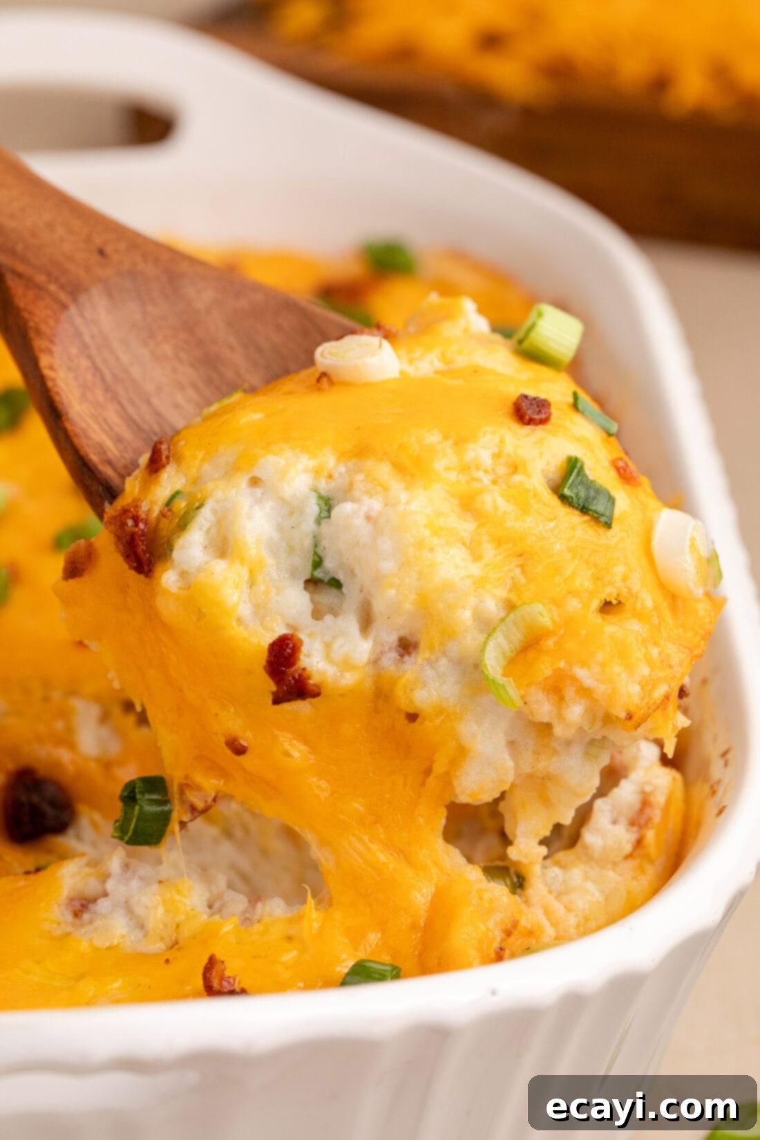 Loaded Cheesy Potato Casserole 2 Spoonful of Twice Baked Potato Casserole being lifted out of the casserole dish, showing layers of creamy potatoes, bacon, and cheese