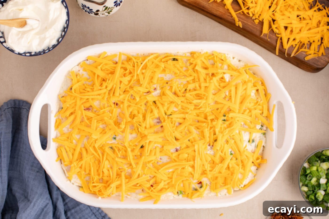 Loaded Cheesy Potato Casserole 12 a layer of shredded cheddar cheese being sprinkled over the top of the potato casserole mixture