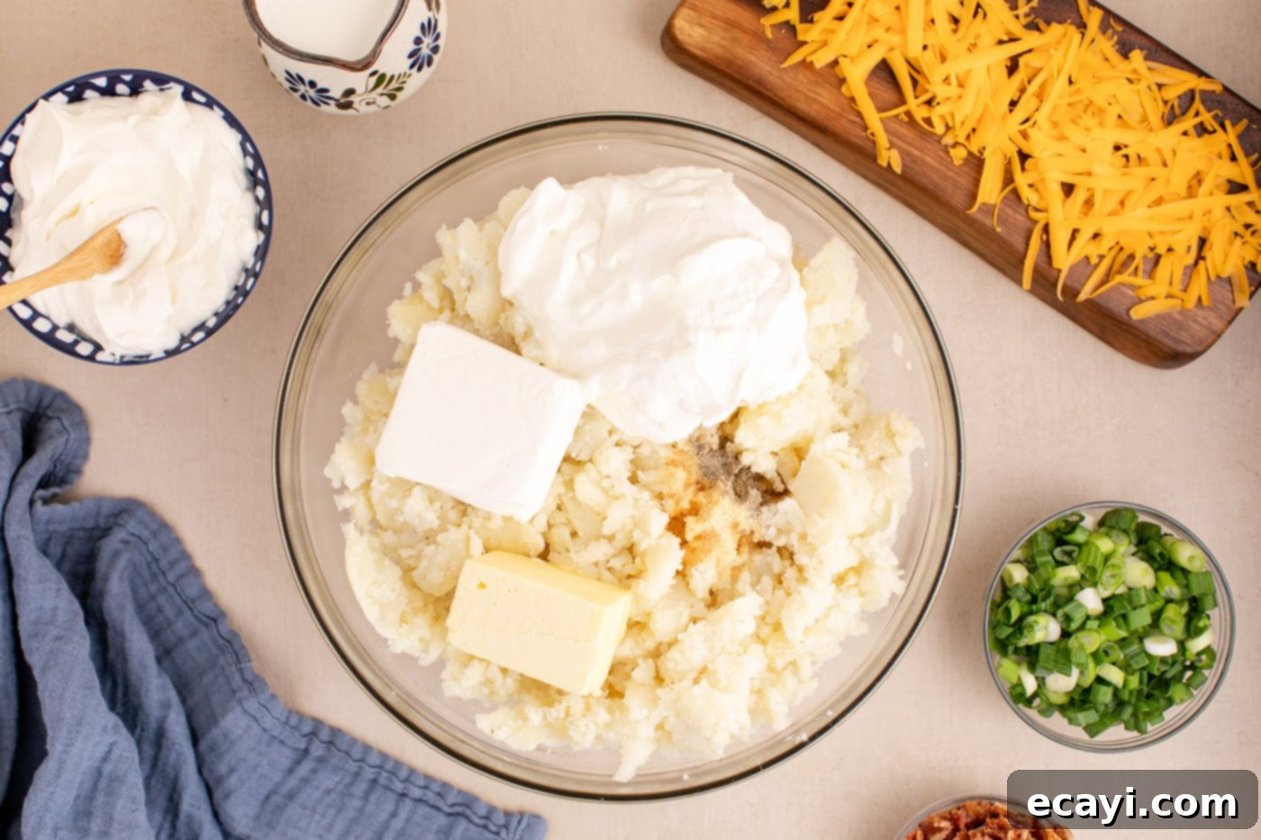 Loaded Cheesy Potato Casserole 7 sour cream, cream cheese, milk, butter, garlic powder, and ground pepper being added to mashed potatoes in a large bowl