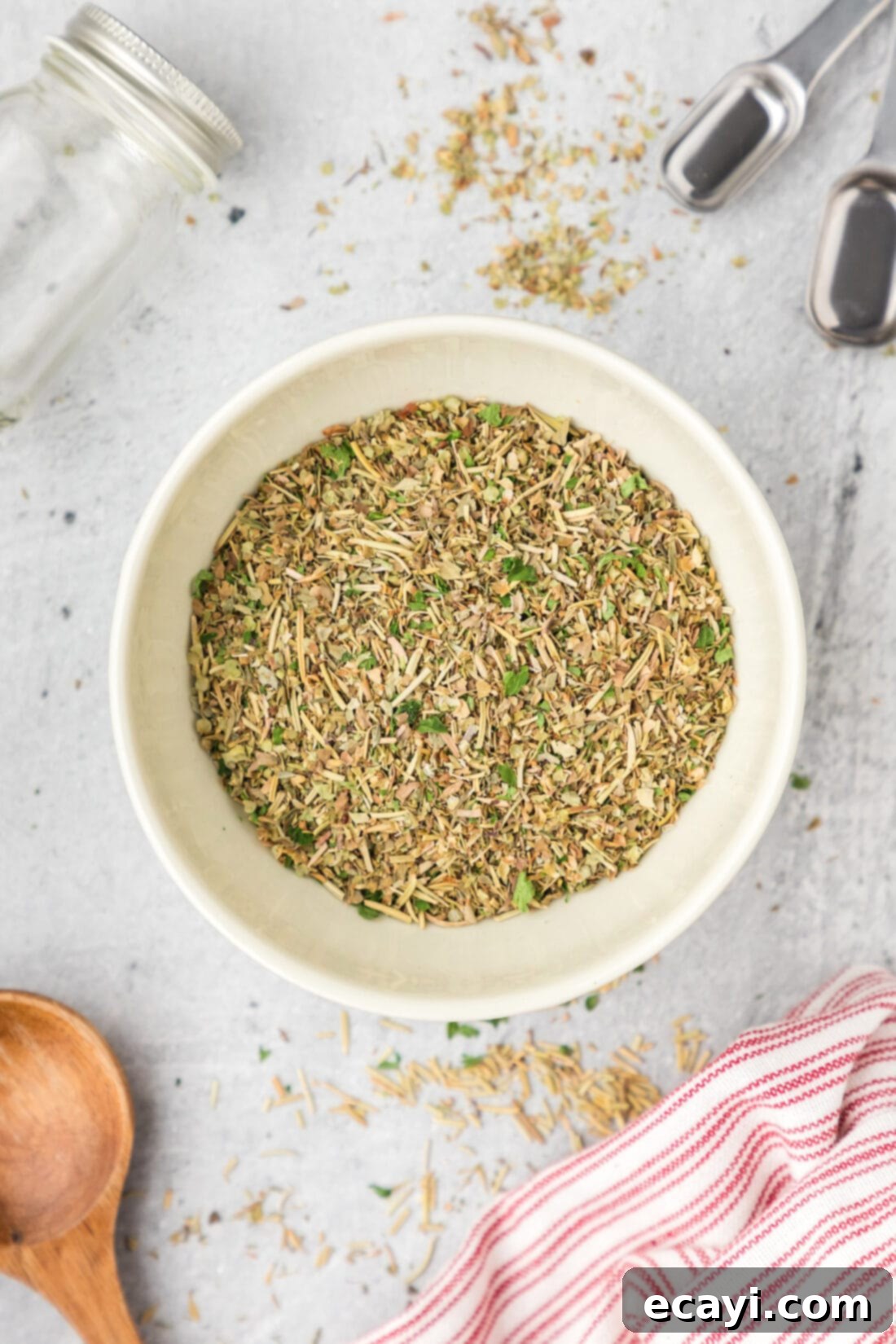 Classic Italian Herb Blend 7 Bowl of Italian Seasoning with measuring spoons and seasoning jar beside it, ready for use.