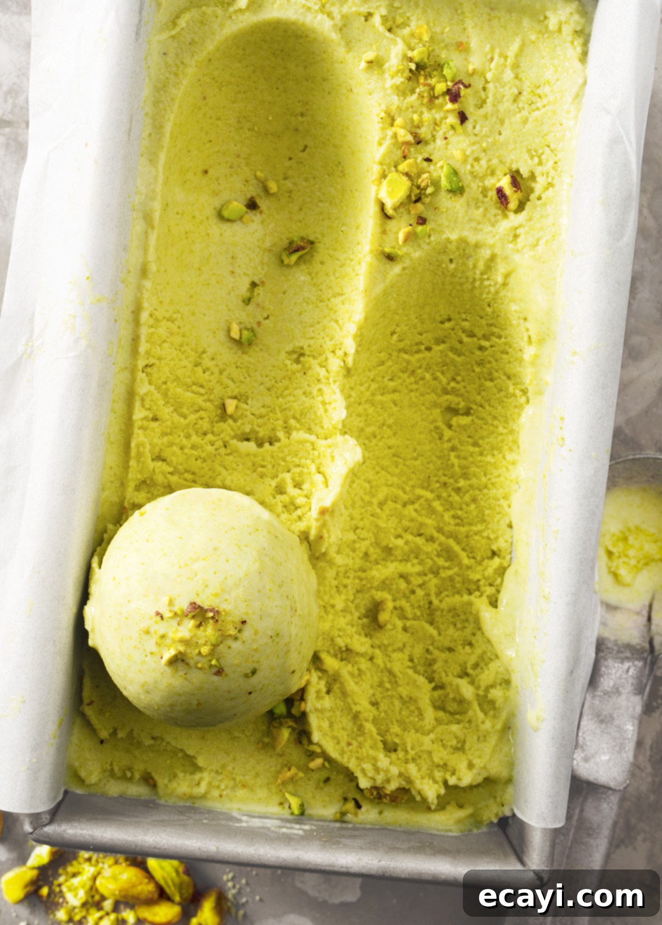 Authentic Pistachio Gelato from Our Homemade Paste 9 A tantalizing close-up of a container brimming with creamy, light green pistachio gelato. A single perfect scoop rests invitingly on the surface, adorned with a sprinkle of crushed pistachios, showcasing its smooth texture and rich flavor. // FoodNouveau.com