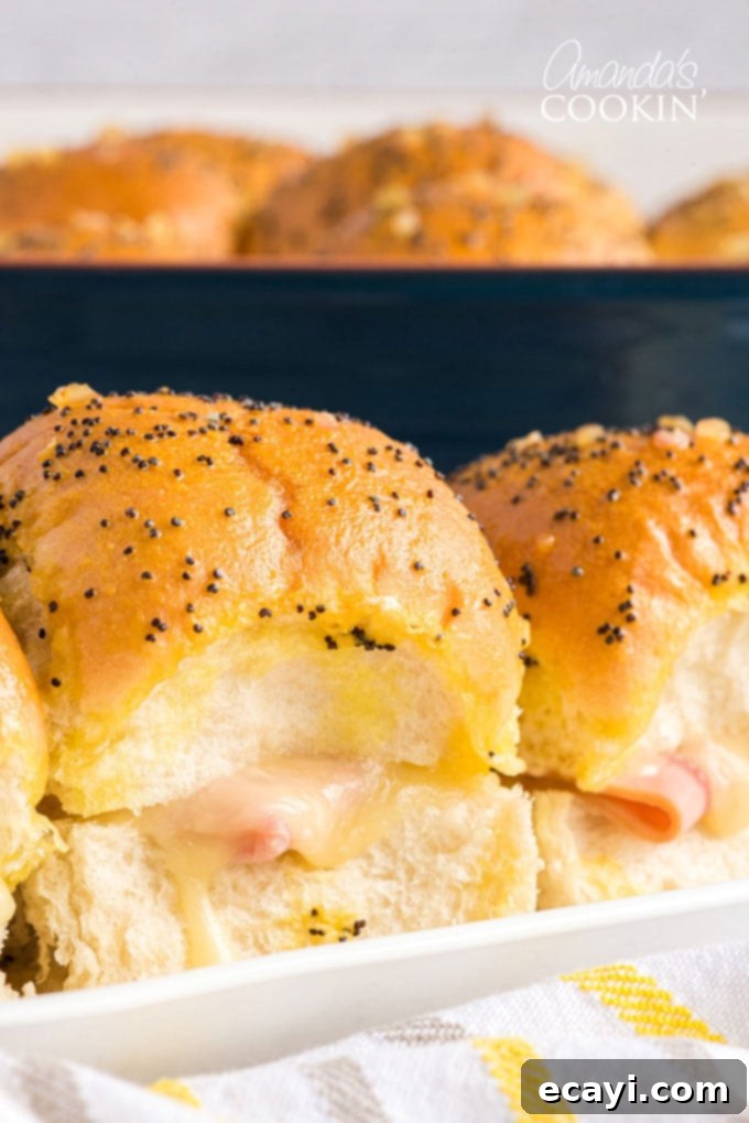 Ham and Cheese Sliders are the perfect appetizer for football parties, potlucks, New Year's Eve, or any other reason to get together and celebrate! Close-up of a single golden-brown ham and cheese slider with melted cheese.