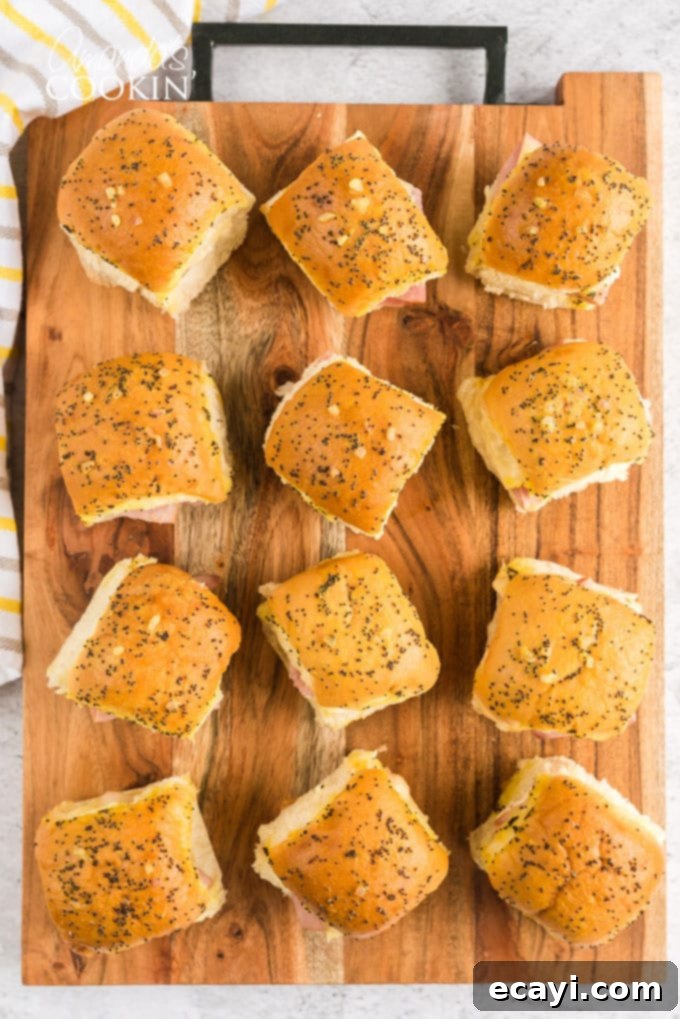 Ham and Cheese Sliders are the perfect appetizer for football parties, potlucks, New Year's Eve, or any other reason to get together and celebrate! A cutting board filled with multiple baked ham and cheese sliders, garnished and ready to serve.