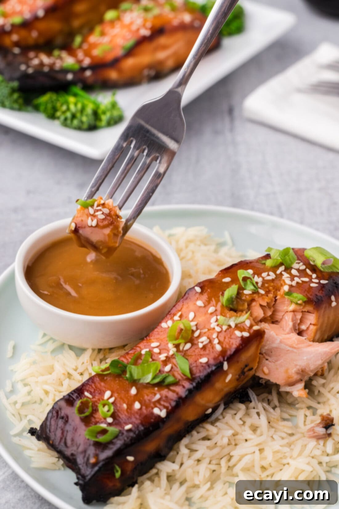 Miso Glazed Salmon 6 Close-up of a piece of Miso Salmon being dipped into a small bowl of miso sauce, highlighting the glaze and flaky texture