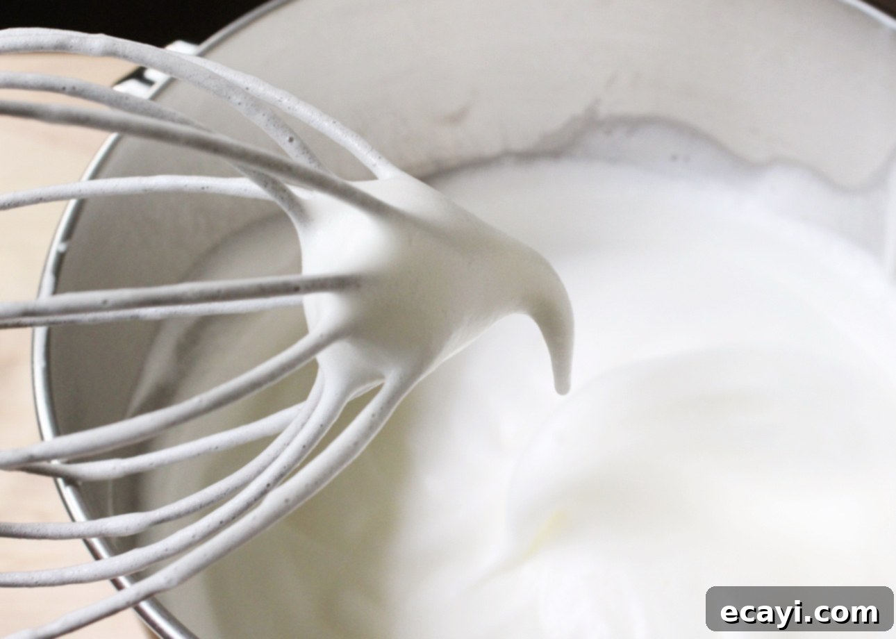Heavenly Homemade Angel Food Cake 10 A metal whisk lifts glossy, stiff peaks of whipped egg whites from a mixing bowl, showing the smooth, airy texture. // FoodNouveau.com
