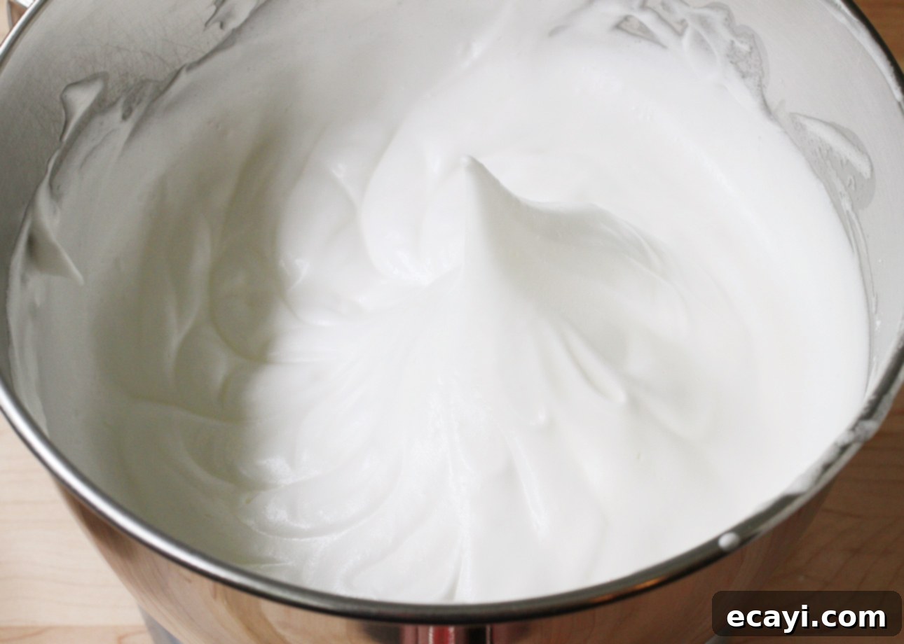 Heavenly Homemade Angel Food Cake 11 A metal mixing bowl filled with glossy, white whipped egg whites forming a stiff peak in the center. The texture appears smooth and airy, indicating the egg whites are well-beaten. // FoodNouveau.com