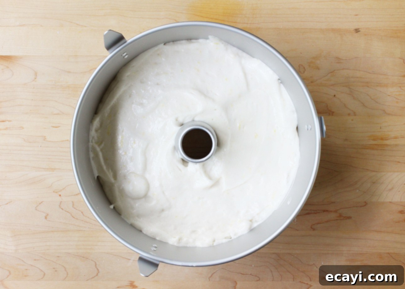 Heavenly Homemade Angel Food Cake 14 A round tube pan filled with smooth, white homemade angel food cake batter sits on a light wooden surface, ready to be baked. // FoodNouveau.com