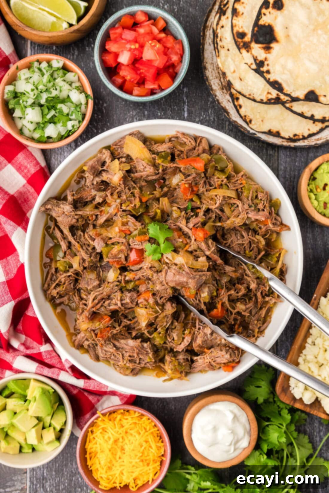 Golden Crispy Beef Carnitas 2 Tongs in a bowl of Beef Carnitas, showcasing its tender, shredded texture amidst colorful vegetables