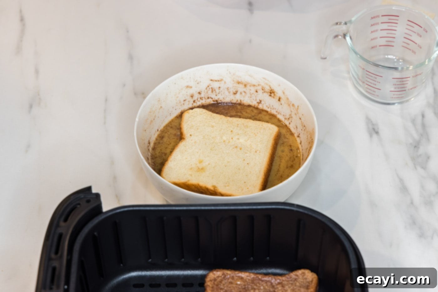 Perfect Air Fryer French Toast 7 A hand carefully dipping a slice of Texas toast into the prepared egg mixture, ensuring full saturation.