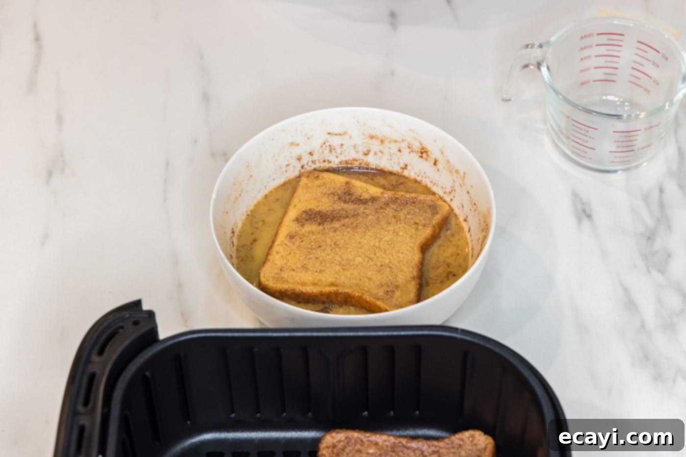 Perfect Air Fryer French Toast 8 A bread slice being lifted from the egg mixture, perfectly coated and ready for the air fryer.