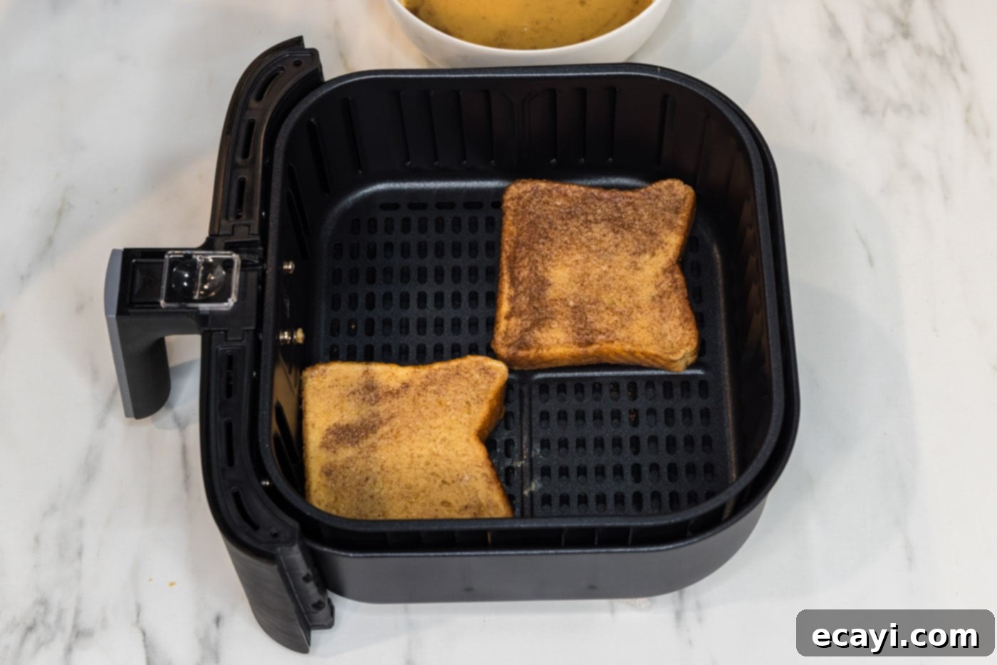 Perfect Air Fryer French Toast 9 Two slices of French toast perfectly arranged in the air fryer basket, ready for cooking.