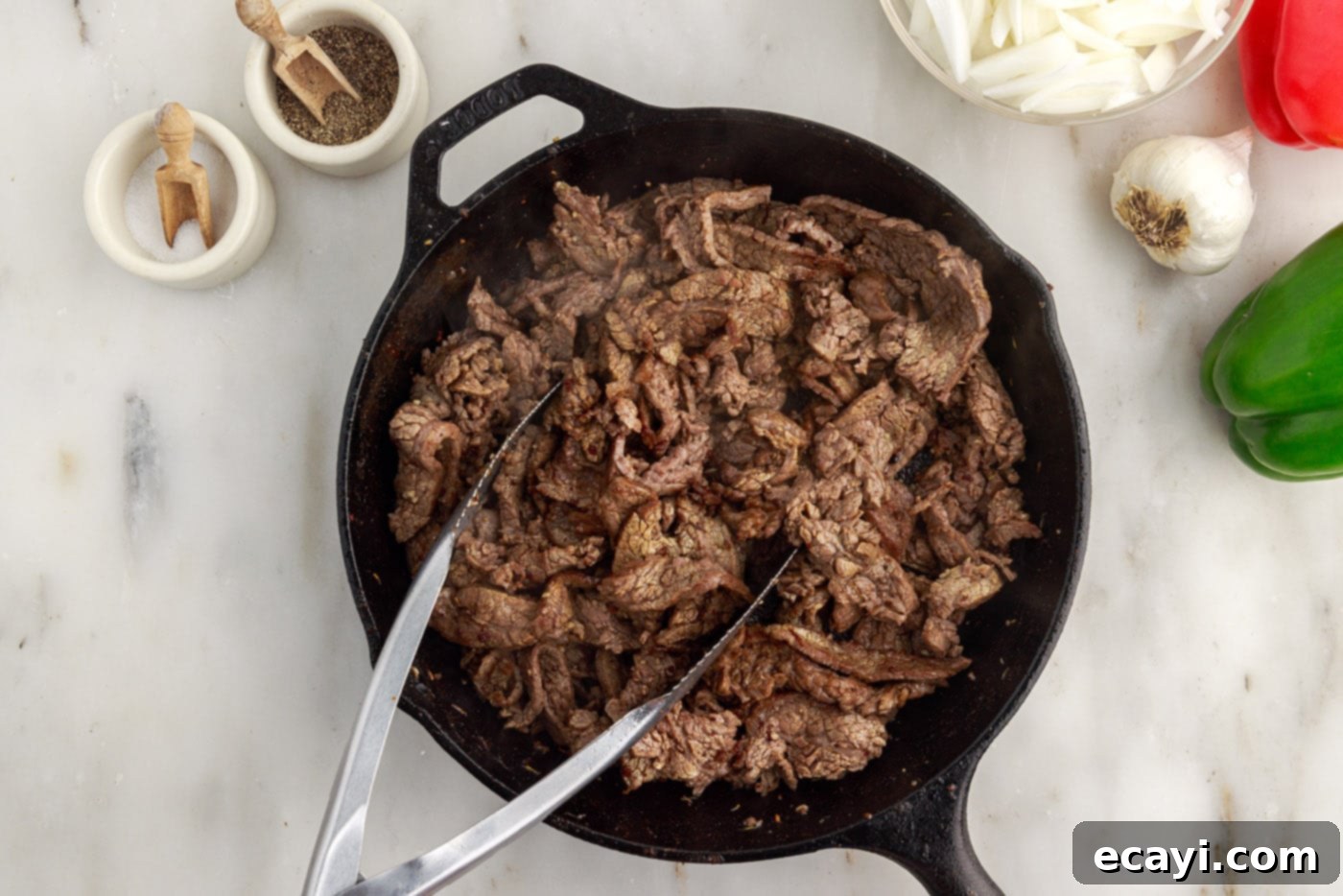 Hearty Philly Cheesesteak Casserole 8 cooked flank steak slices resting in a cast iron skillet