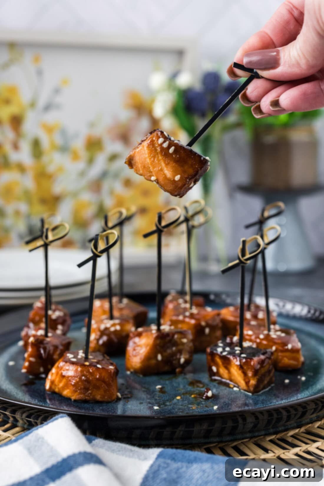 Salmon Morsels 2 Hand holding up a perfectly cooked Honey Soy Salmon Bite on a pick, showcasing its crispy exterior and glistening marinade.