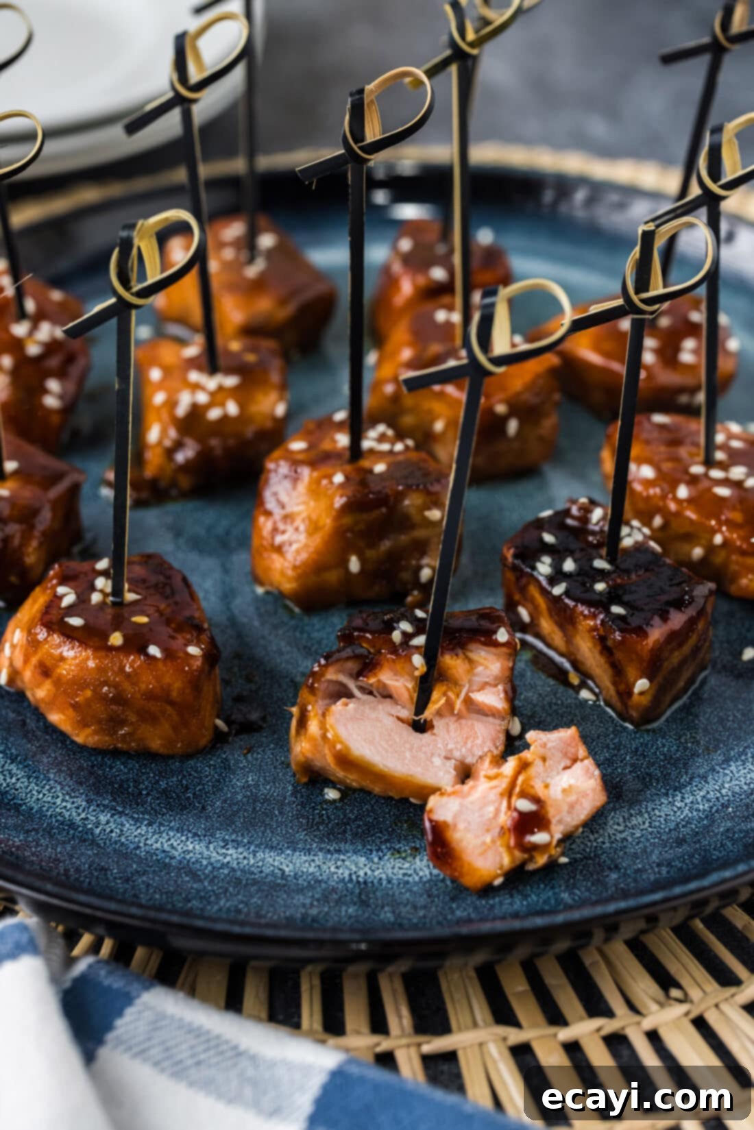 Salmon Morsels 3 Cooked Salmon Bites broken apart on a plate, revealing the flaky, tender interior, with more glazed salmon cubes visible in the background.