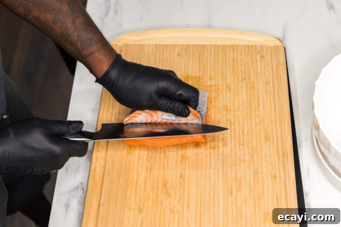 Salmon Morsels 5 Expertly removing skin from a salmon filet with a sharp knife on a cutting board, preparing it for cubing.
